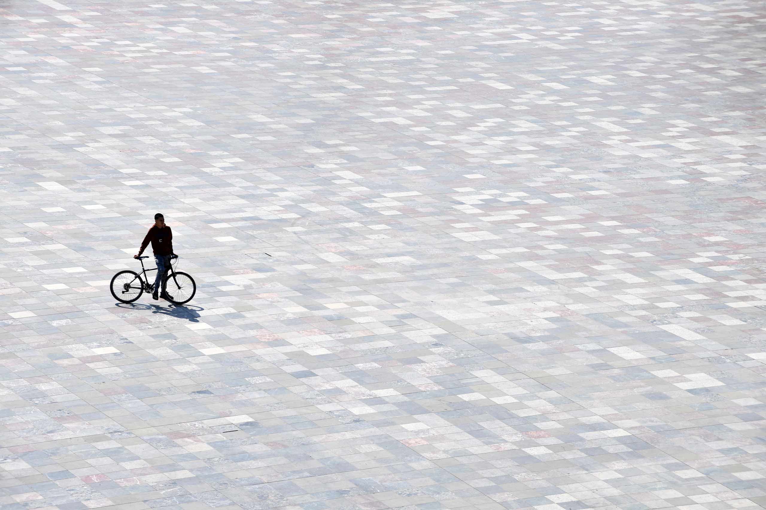 Silhouette of a man alone in a square leaning on his bicycle